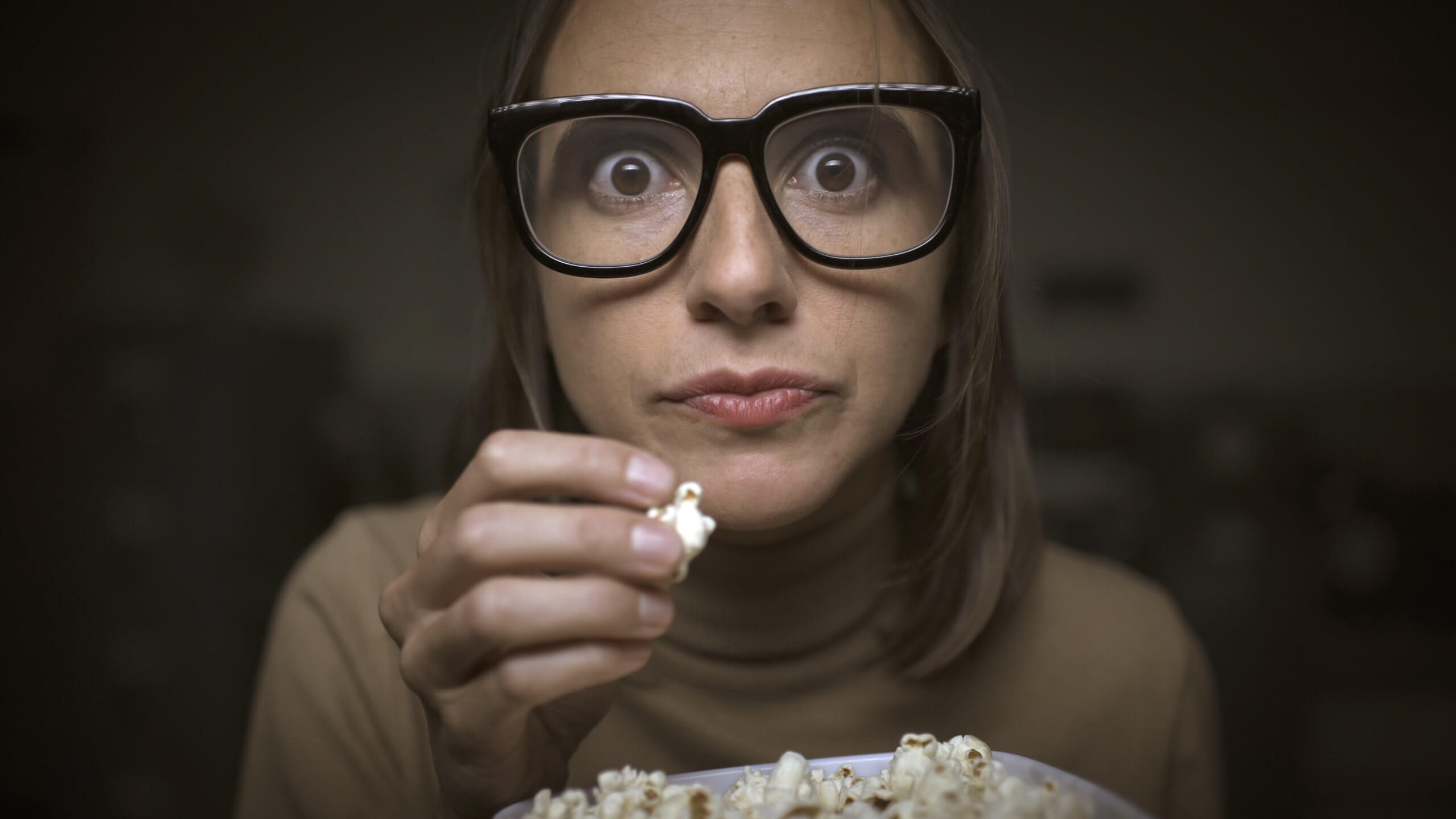 woman with glasses eating popcorn