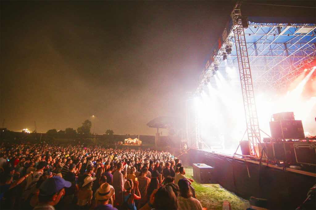 Dozens of fans are pressed together in front of a brightly lit outdoor stage