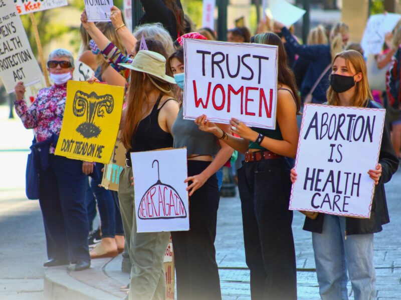 Multiple protestors stand at a rally, holding signs in support of abortion access.