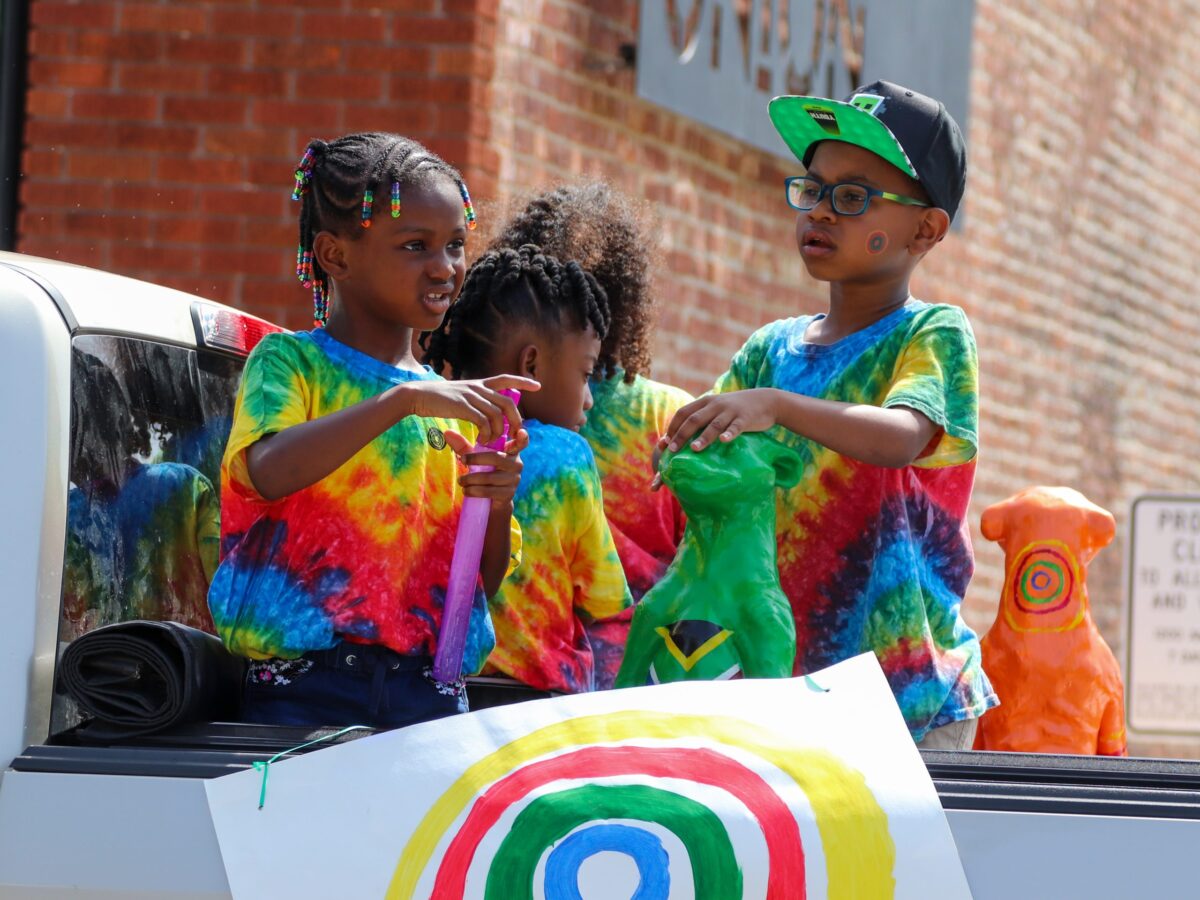Three children from Nelson Mandela Elementary stand in the bed of a pickup truck as a part of the Juneteenth Parade.
