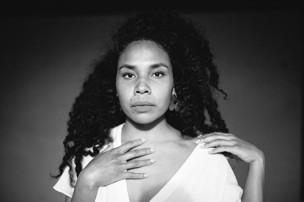 Mary Lawson stands facing the camera, her hands on her shoulders. The photo is in black and white.