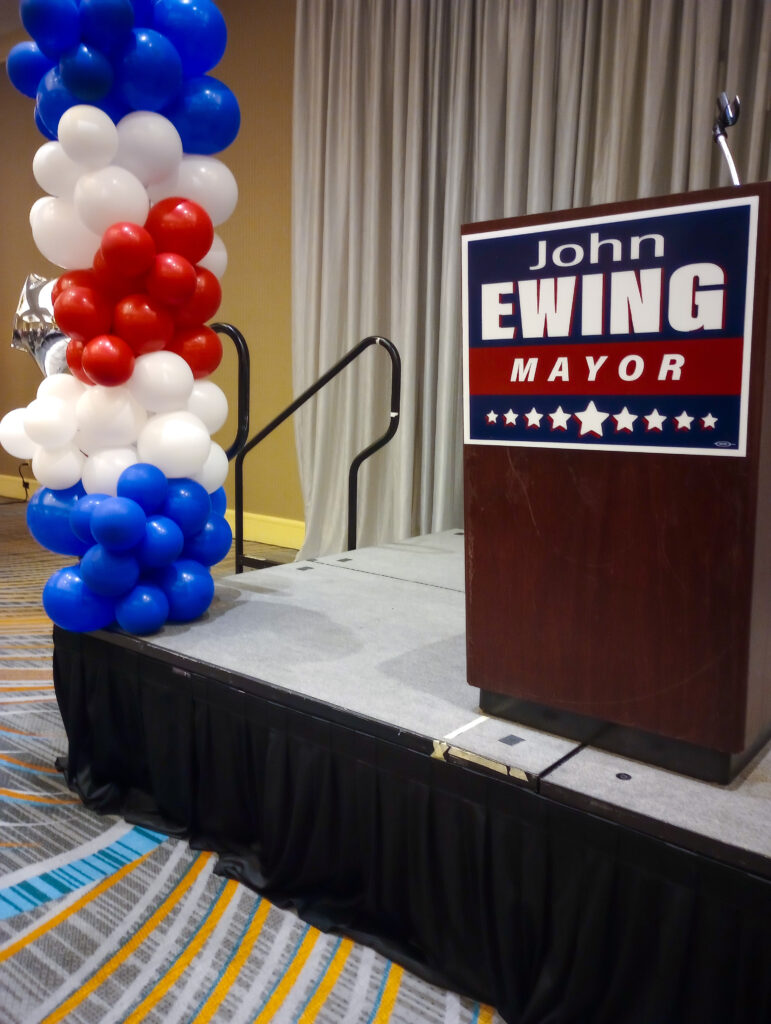 A Ewing for Mayor sign on the front of his podium, next to red, white and blue balloons