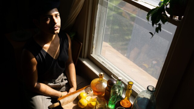 Obed Sanchez-Liborio posing in his room next to glass bottles full of agua de jamaica, water and tequila. Photo by Chris Bowling.