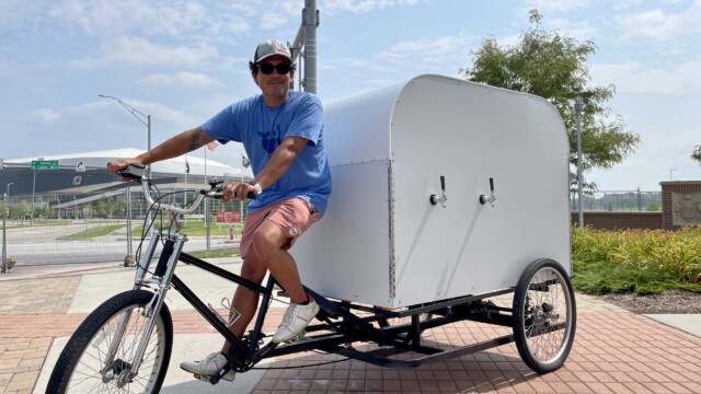 Damian David, a Springo Water representative and an avid Maha fan, smiles at the edge of the festival grounds before he returns to the heart of the event, stopping often for spectators to refill their water bottles from the trailer hitched to his bike. Photo by Bridget Fogarty.